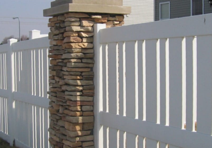 A classic white picket fence paired with a robust stone pillar, symbolizing traditional outdoor aesthetics.